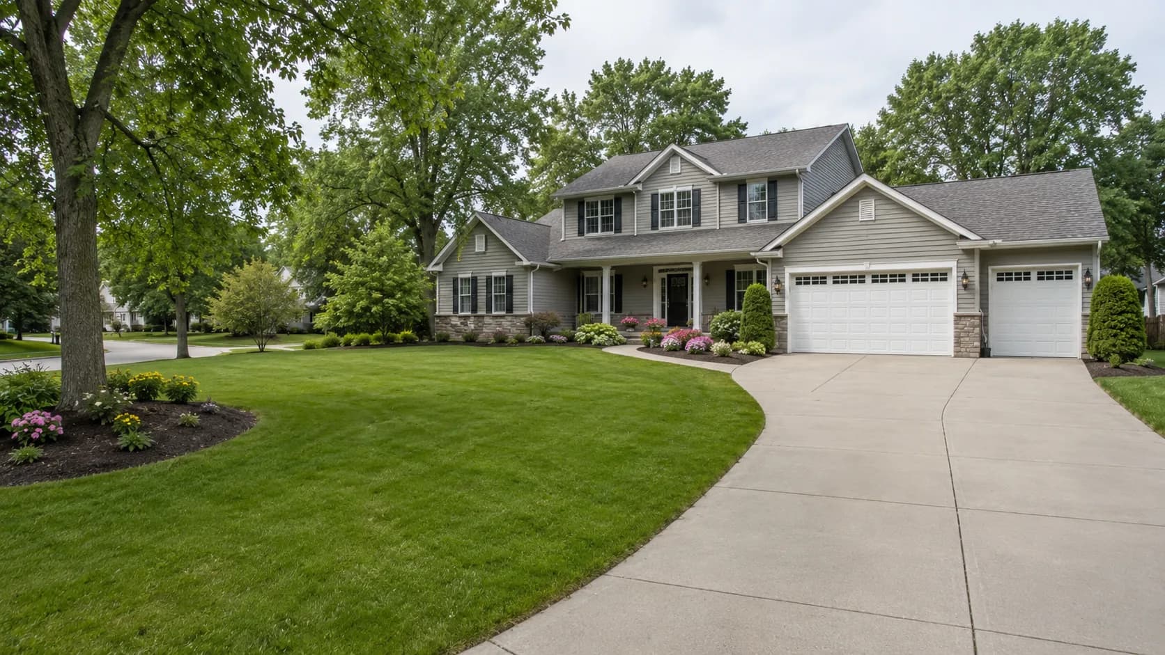 House with a front lawn, planting beds, mature trees and a concrete driveway